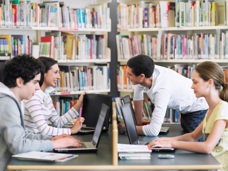 Teenage students using laptops in library